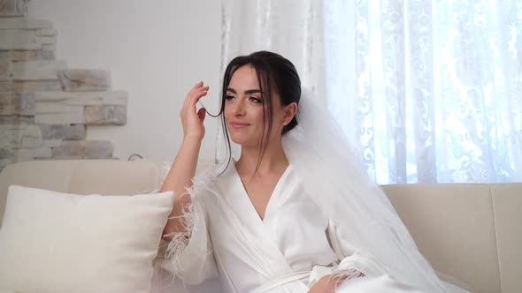 The Brunette Bride is Sitting Thoughtfully on the Couch and Looking Away