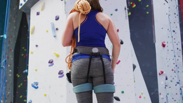 Rear view of caucasian woman with rope over her shoulder at indoor climbing wall