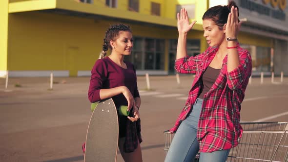 Two Hipster Girls Standing By the Shopping Cart on Parking By the Citymall During Sunset