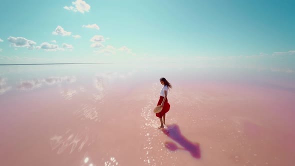 Slow Motion of Laughing Happy Woman Traveler in Red Skirt and Hat Walking in Pink Water with