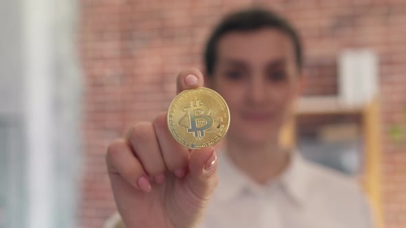 Woman Shows a Gold Bitcoin Coin Closeup While Standing in the Office