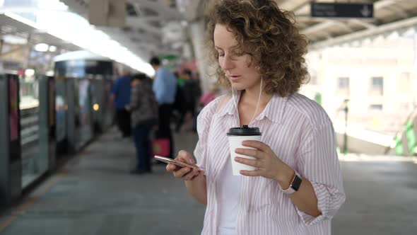 Young Woman Using Smartphone While Waiting For Train On Station Platform
