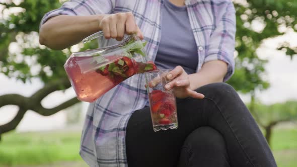 Closeup of Female Hands with Jug Pouring Fresh Natural Drink with Strawberries and Mint Into Glass