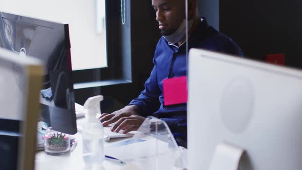 African american man with lowered face mask using computer at modern office