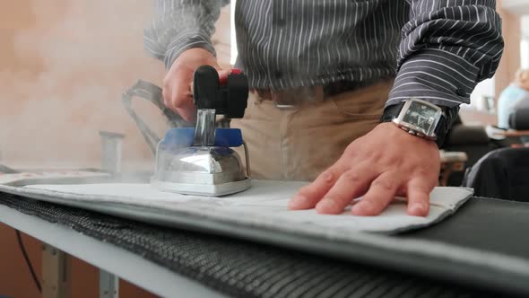 Man irons clothes on ironing board with blue steaming iron