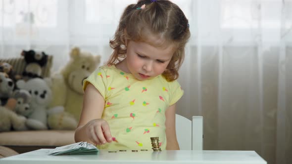 Child girl counts her savings and puts coins in a stack. Concept of kids economy, saving money.