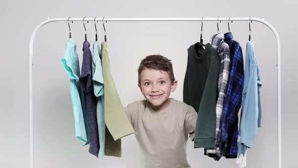 The little boy appears from behind the clothes rack. The boy looks through his shirts on hangers.