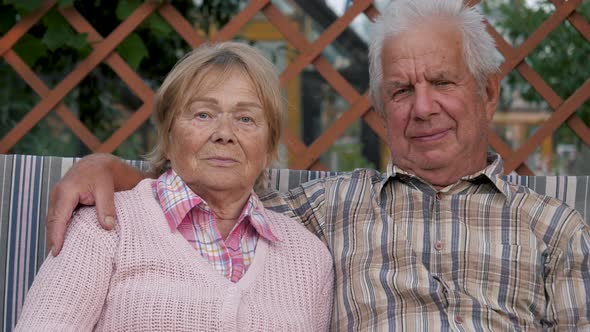 Portrait Elderly Couple Sitting On Swing In Garden Hugging