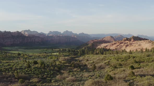 Low flying over green grassy field with expansive view of rocky cliffs within Zion National Park