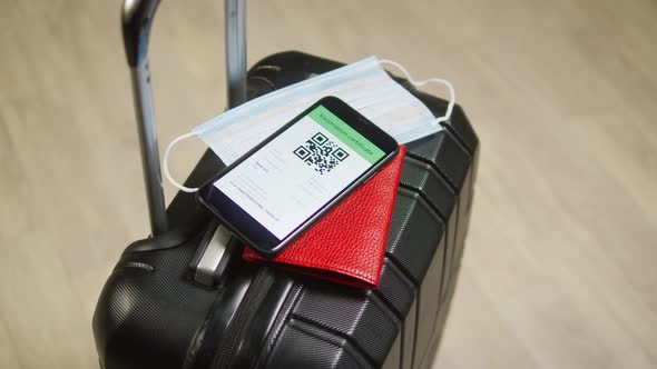 QR Code on Smartphone Medical Mask and Passport on Suitcase