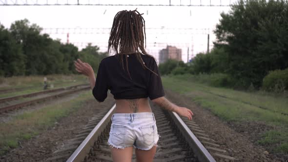 A Young Attractive Woman with Dreadlocks is Walking Along the Railroad