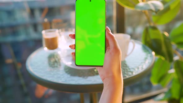 Woman Sitting in a Cafe and Using Smartphone with Green Mockup Screen in Vertical Mode