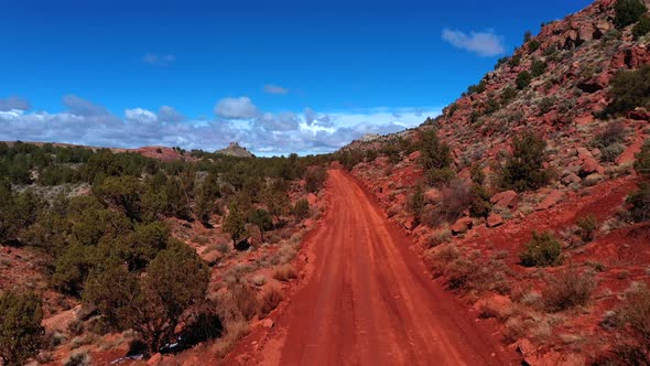 A drone flying along a dusty road on a hilly terrain in an arid wilderness on a sunny day. outside k