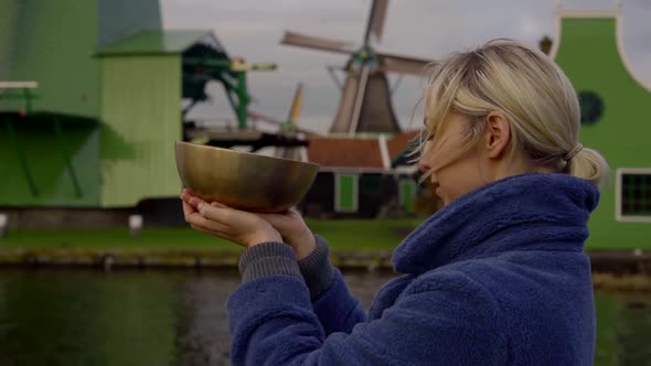 Blonde Woman Is Holding Vibrating Resting Bell in Hands in Background of Dutch Mills