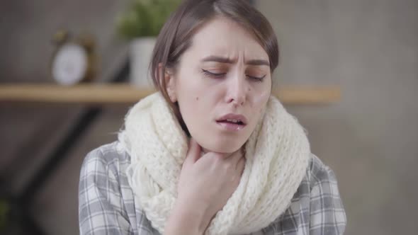 Portrait of Coughing Caucasian Brunette Woman in White Scarf. Pretty Sick Girl Spending Day at Home