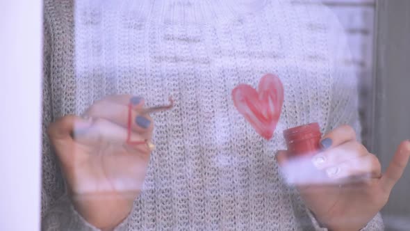 Female Hand Draws Red Heart Word LOVE on the Window with Paint