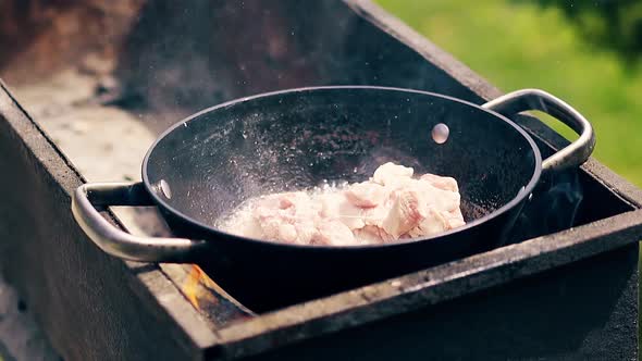 Close-up, Slow Motion: Pork Meat Is Fried in Saucepan on Charcoal. The Person Adds Meat To the