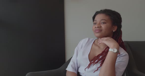 Cute Afro Woman Sitting in Armchair and Smiling Leaning on Her Hand