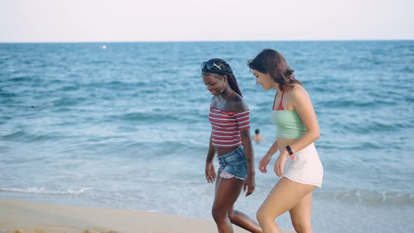 Two Multiracial Friends Walking Along Surf Line