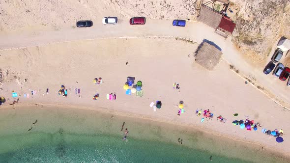 Flying above parked cars and people on sandy beach of Pag island