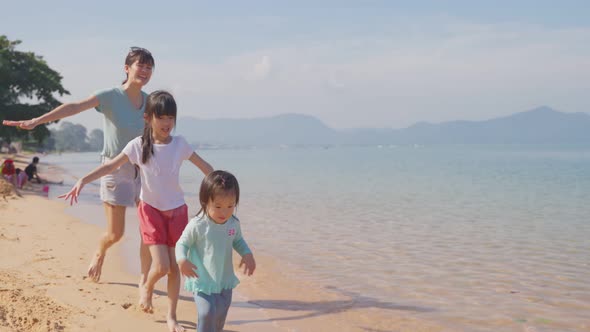 Happy Asian family, Mother playing and having fun with children on the beach during holiday vacation