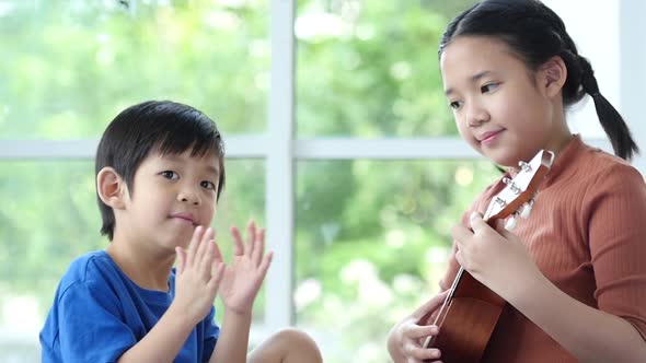 Asian Children Playing Ukulele Together In Living Room