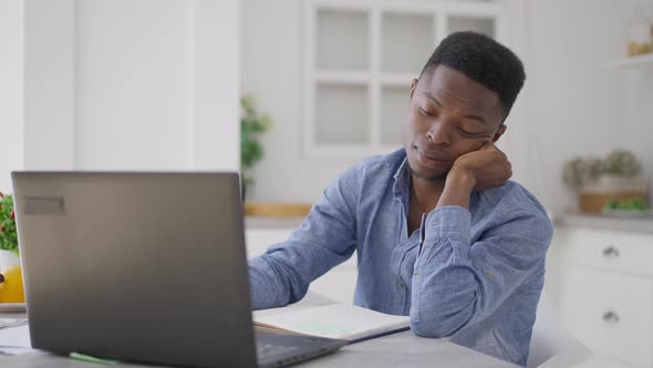 Tired Exhausted Young Man Falling Asleep Sitting at Kitchen Table in Home Office