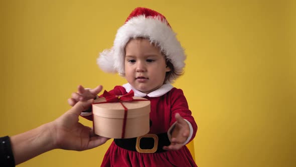 Happy Cheerful Chubby Toddler Baby Girl in Santa Suit Looking On Camera At Yellow Background