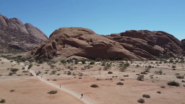 Long road next to a massive round rock, people are walking in a desert, Namibia