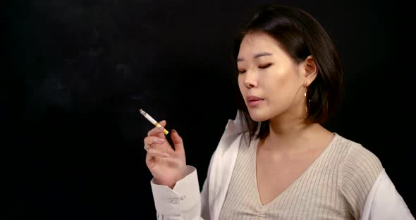 Nervous Asian Woman Is Smoking in Black Background, Portrait