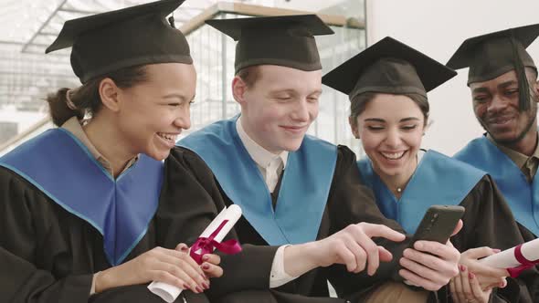 Four Young Graduates Looking at Telephone Screen and Laughing