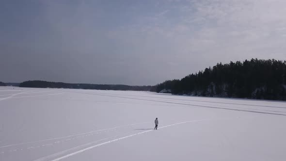 Aerial shot of lonesome young woman walking on a frozen lake enjoying the great outdoors.