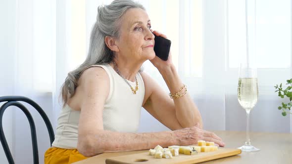 Beautiful Old Grandmother with Grey Hair and Face with Wrinkles is Using Smartphone Talking with