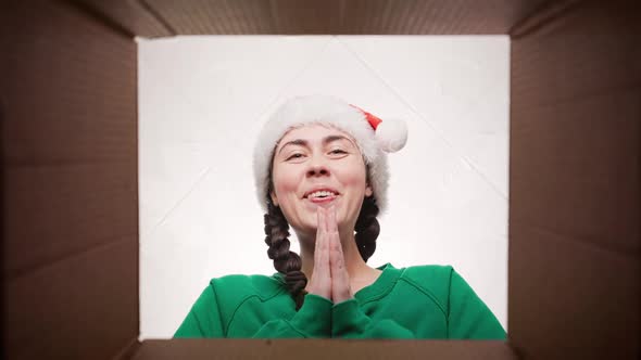 Portrait of a young happy cheerful woman in a Christmas hat opening a parcel.