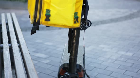 Pedestal Shot of Electric Scooter on City Street with Yellow Food Delivery Backpack Hanging on