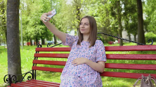 Pregnant Woman in a Summer Dress with a Floral Print Walks in the Park