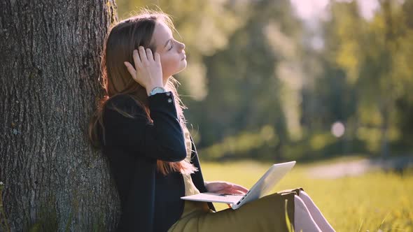 A Girl with a Laptop Resting in the Park By a Tree