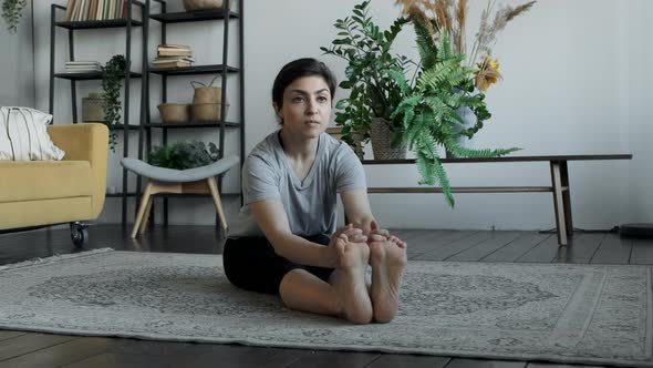 Young Indian Woman Meditates sitting on the Carpet and Doing Stretching, doing Yoga