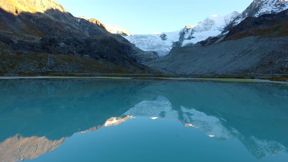 Flying low over small lake with reflecting mountains and glacier at sunset light