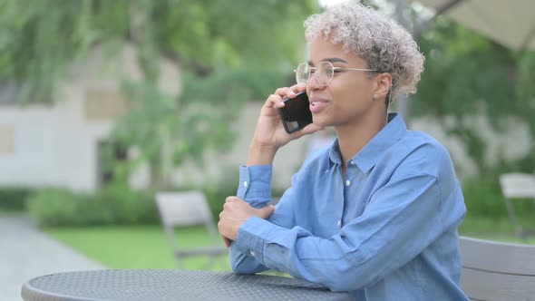 Young African Woman Talking on Phone in Outdoor Cafe