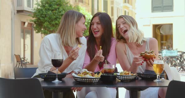 Cheerful women having meal with drinks in summer cafe