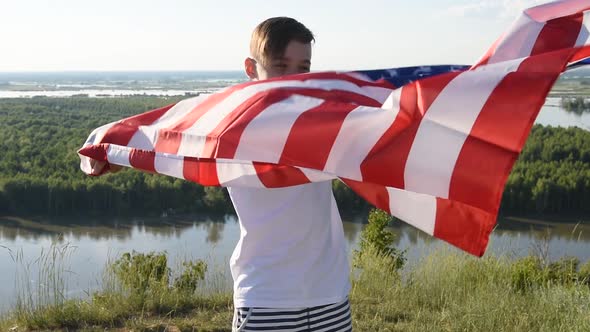 Blonde Boy Waving National USA Flag Outdoors Over Blue Sky at the River Bank