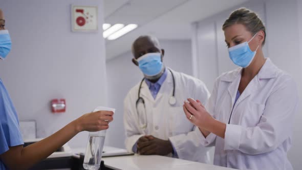 Diverse hospital worker disinfecting hands of doctors all wearing face masks