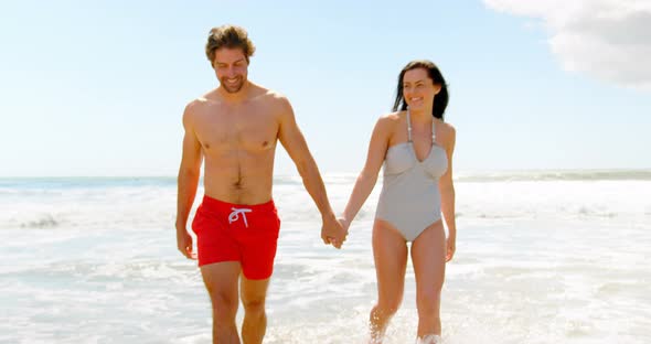 Front view of young caucasian couple walking hand in hand at beach 4k