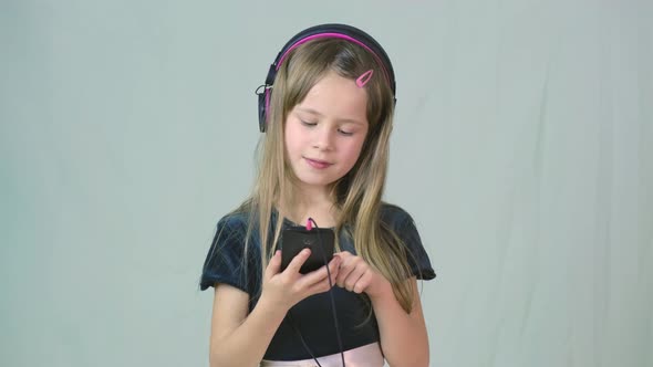 Pretty Smiling Cild Girl Listening to Music in Big Pink Earphones