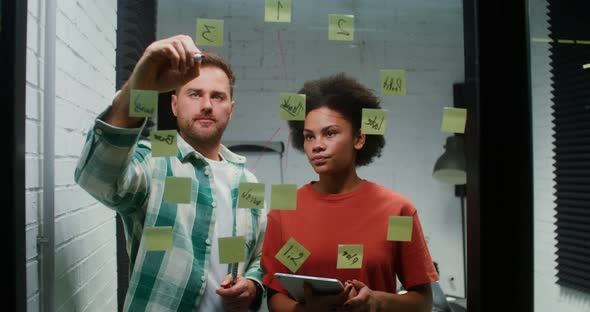 A Young Man and Woman are Planning in the Office Drawing on a Glass Board