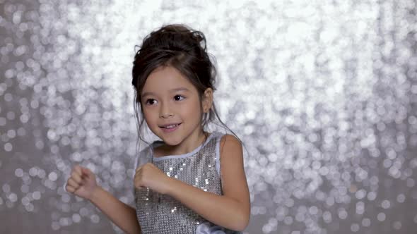 Cute Happy Little Girl Child in a Silver Dress Dancing on Background of Silver Bokeh