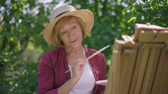 Smiling Senior Caucasian Woman Painting on Easel in Slow Motion Standing in Sunshine Outdoors