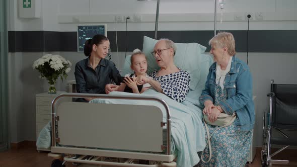 Old Man and Niece Browsing Internet on Smartphone in Hospital Ward Bed