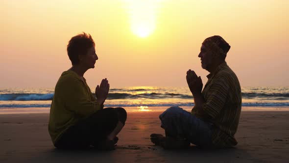 Senior Couple Sits and Meditating Together on Sandy Beach
